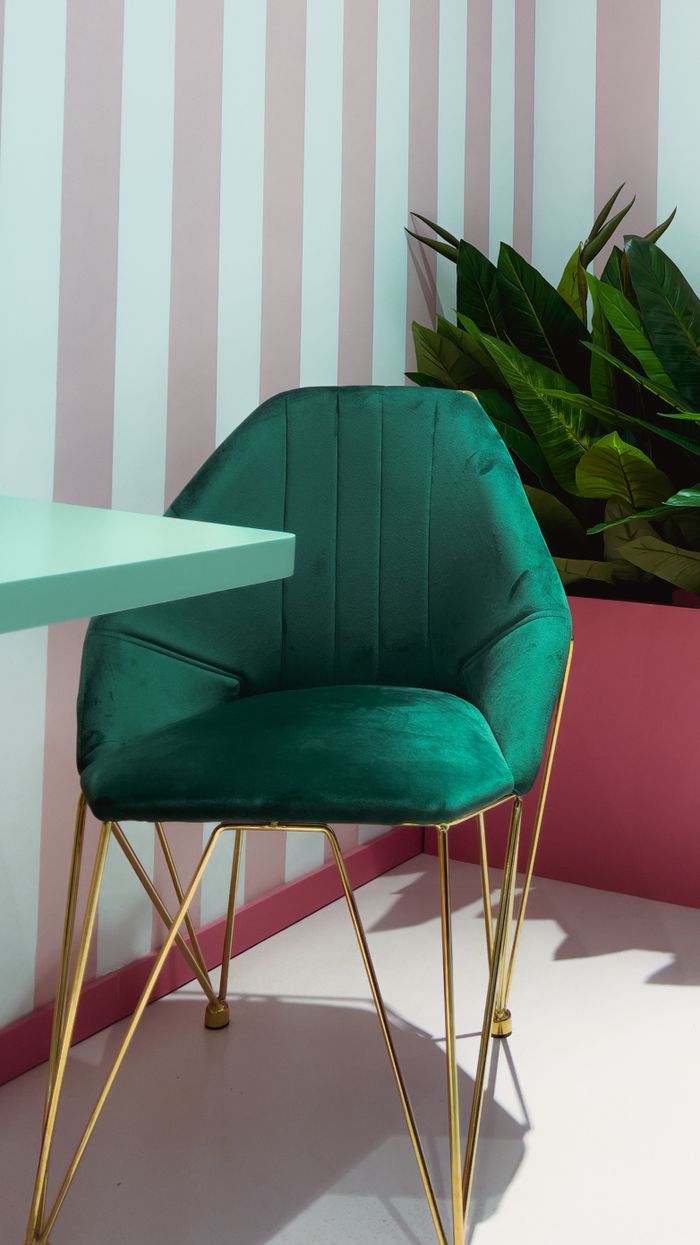 Home Sophisticated green velvet chair with gold legs in a chic interior setting enhanced by striped walls.